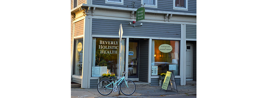 The Beverly Holistic Health practice at 146 Cabot Street in Beverly, Massachusetts, a grey clapboard storefront with gold lettering on the window and a hanging sign.