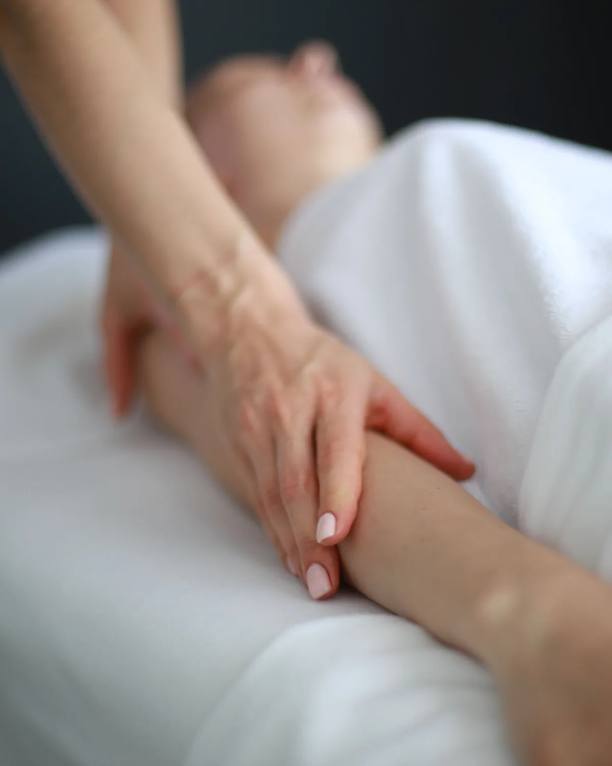 A massage therapist working along a client&rsquo;s forearm over white linen during a treatment.
