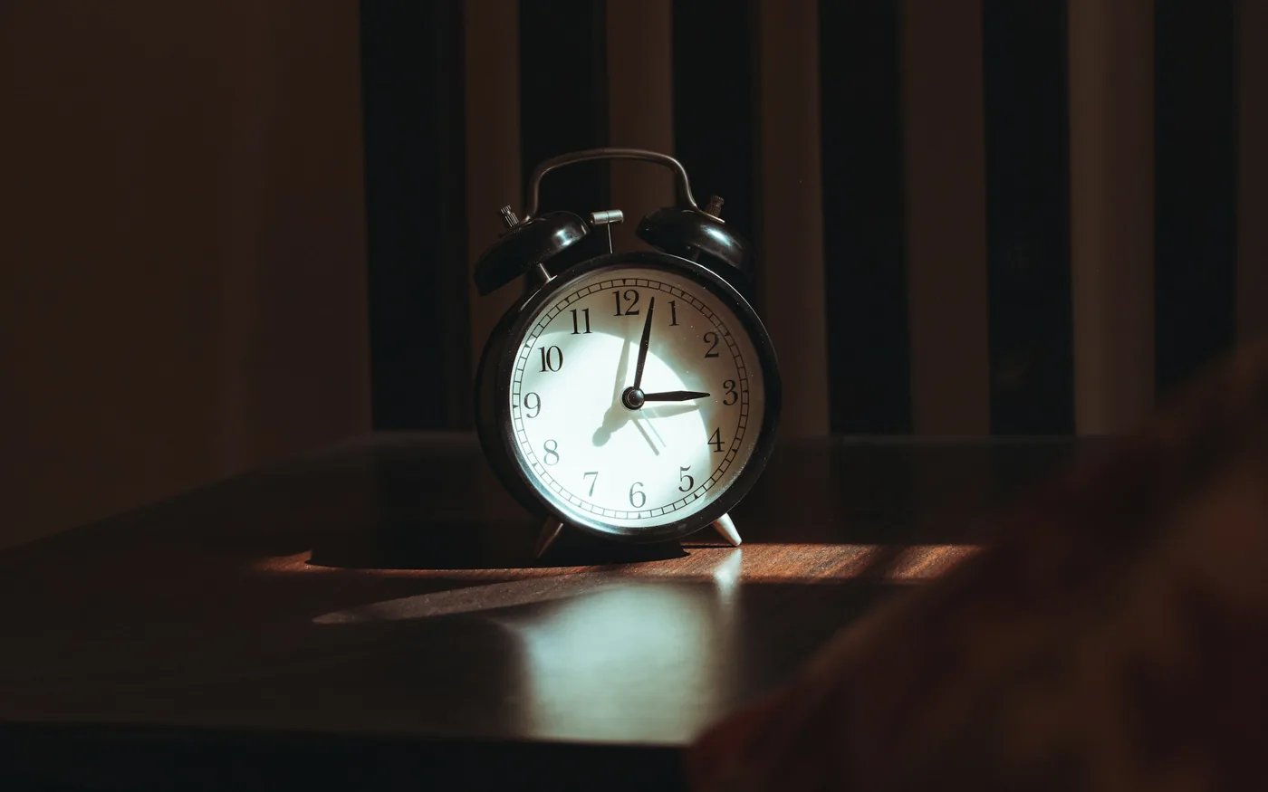 An alarm clock beside a bed &mdash; irregular sleep is one of the most common migraine triggers